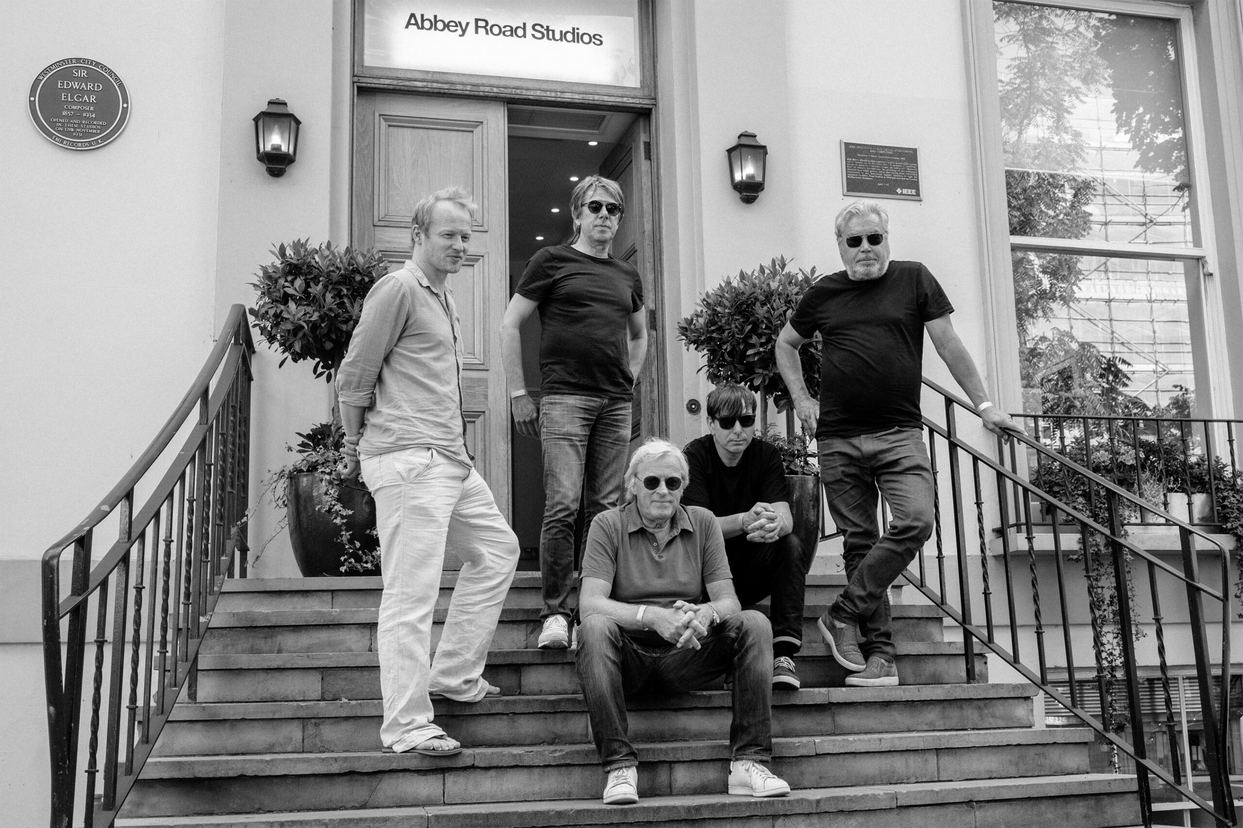 Die Band sitzt und steht auf der Treppe vor den Abbey-Road-Studios