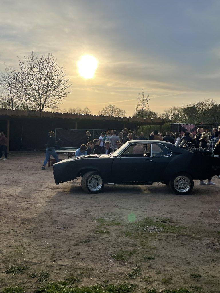 Das selbstgebaute „Batmobil“. Im Hintegrund spielen Besucher:innen Tischtennis, andere warten gespannt darauf, dass es losgeht.