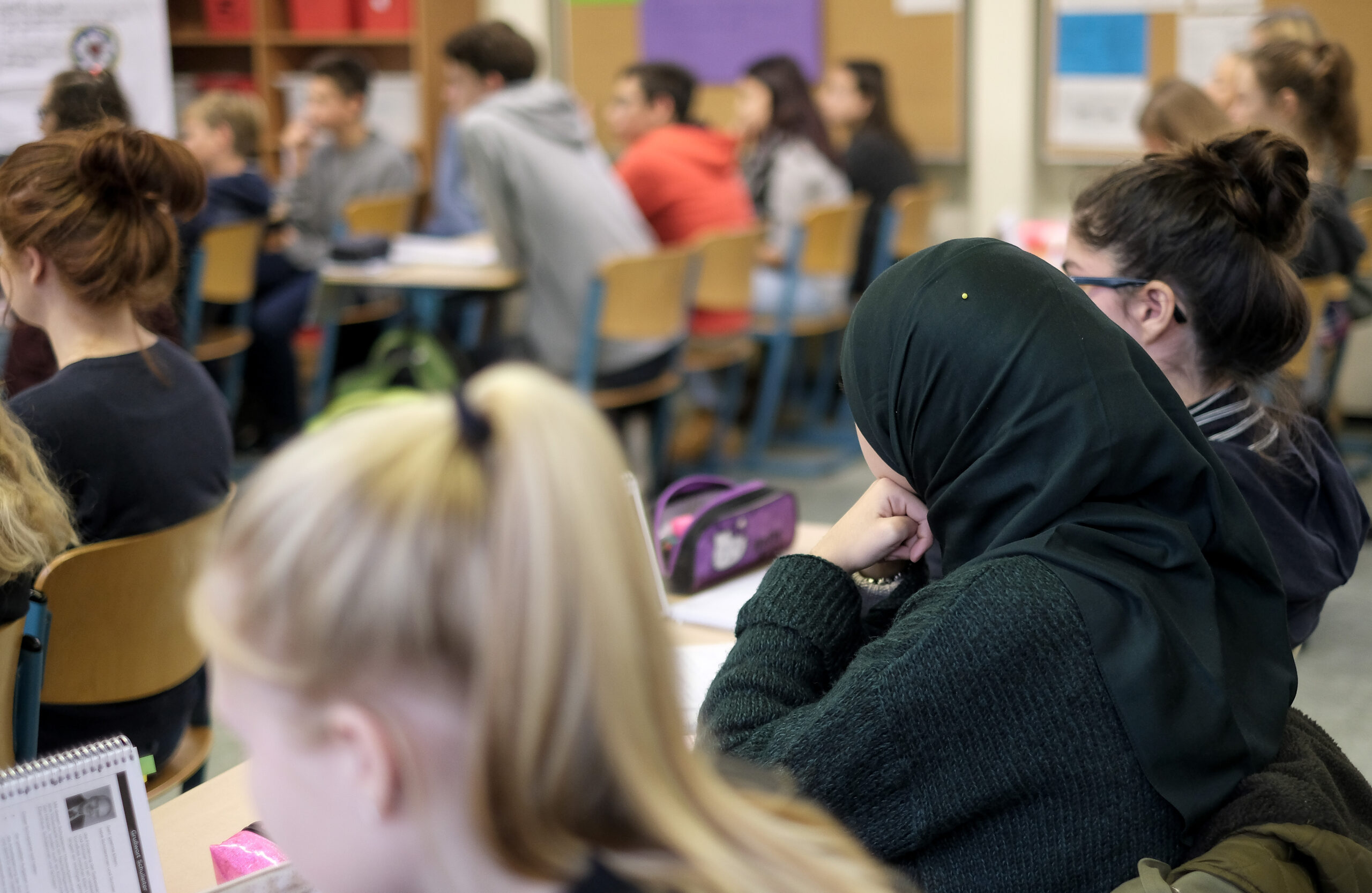 Eine Schülerin mit Kopftuch sitzt zwischen ihren Mitschülern in ihrer Klasse.
