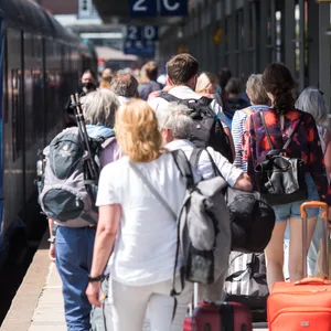Symbolbild: Reisende gehen auf der Nordseeinsel im Bahnhof Westerland an einem Zug der Deutschen Bahn entlang.