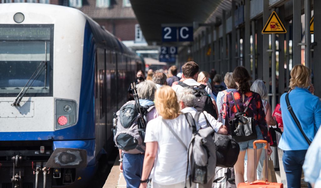 Symbolbild: Reisende gehen auf der Nordseeinsel im Bahnhof Westerland an einem Zug der Deutschen Bahn entlang.