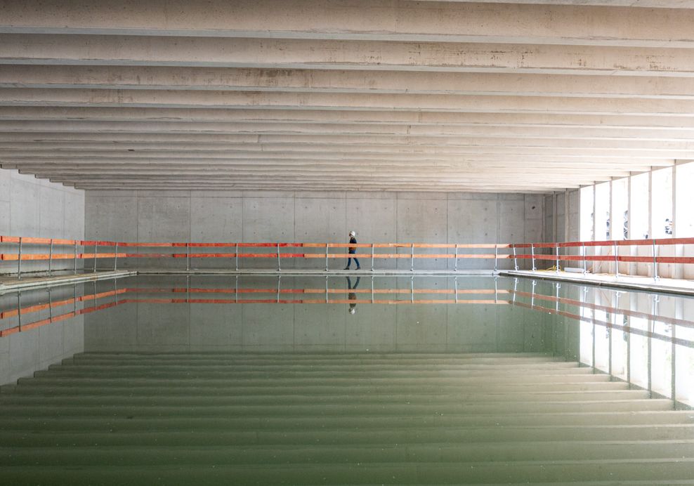 Eine Frau geht während einer Besichtigung der Baustelle der Alster-Schwimmhalle an einem Schwimmbecken entlang.