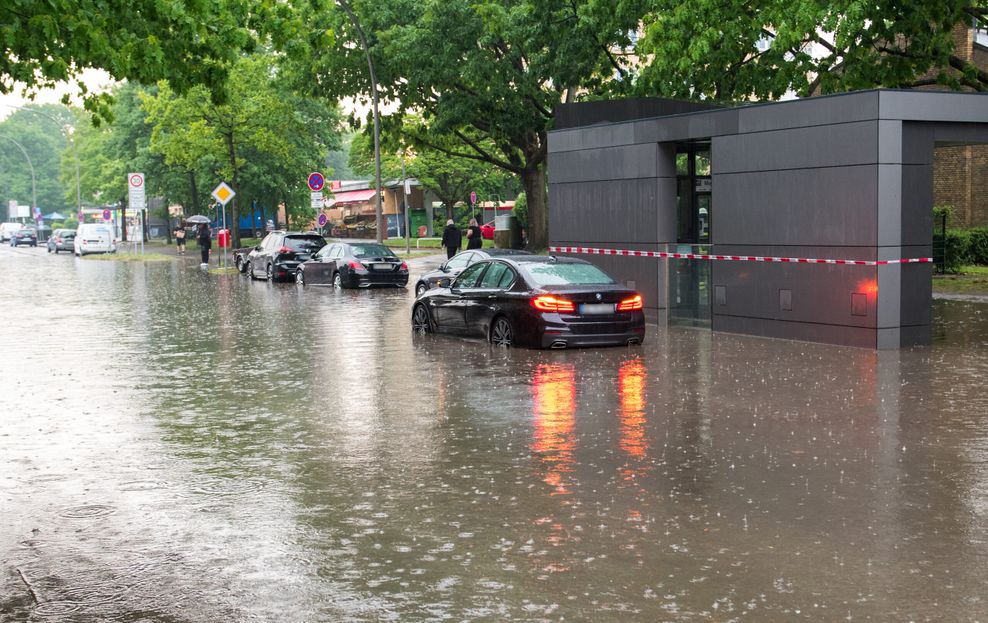 Ein Auto steht im Stadtteil Öjendorf auf einer von starkem Regen überfluteten Straße im Wasser.