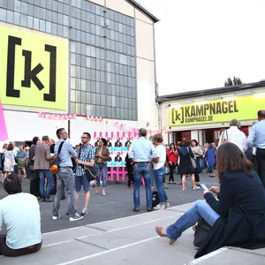 Kampnagel-Außengelände. Während des Sommerfestivals stehen und sitzen Menschen vor den Hallen