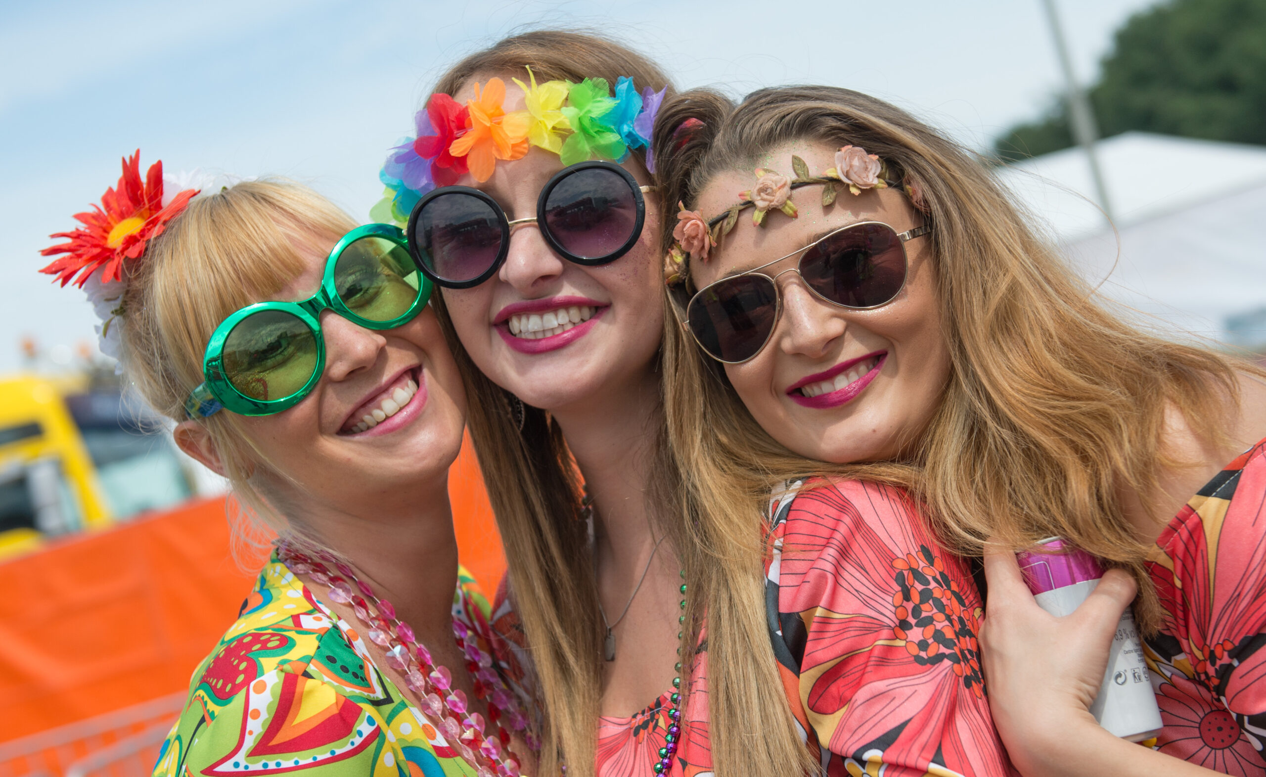 Drei Frauen mit Sonnenbrillen und bunten Kostümen grinsen in die Kamera