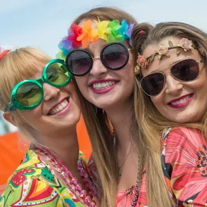 Drei Frauen mit Sonnenbrillen und bunten Kostümen grinsen in die Kamera