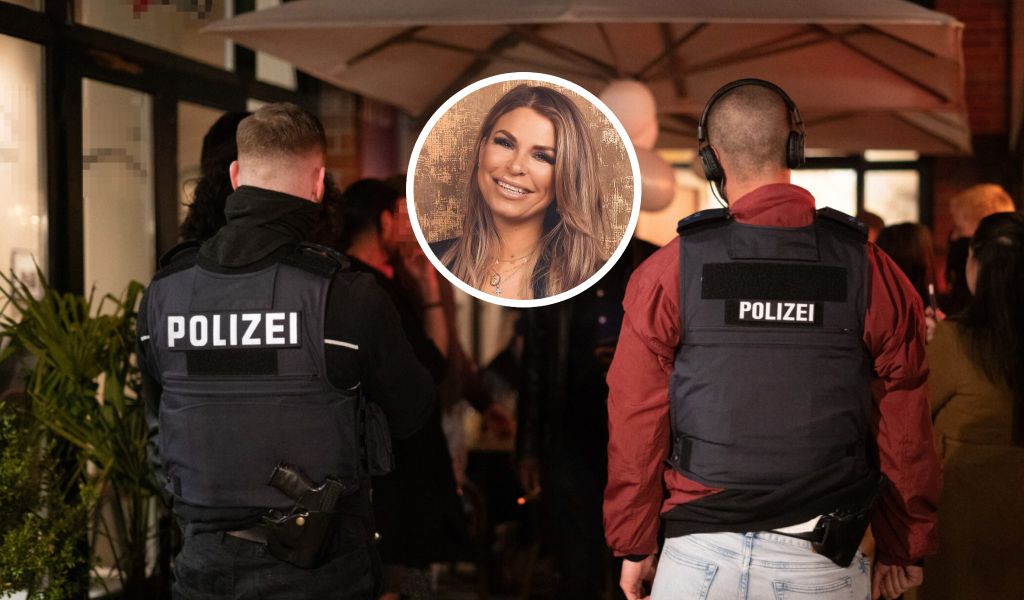 Zwei Polizisten stehen am Außenbereich eines Lokals, eingeklinkt eine lächelnde Frau
