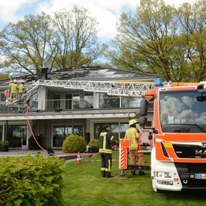 Ein Einsatzwagen der Feuerwehr steht vor einem Haus mit ausgebranntem Dachstuhl.