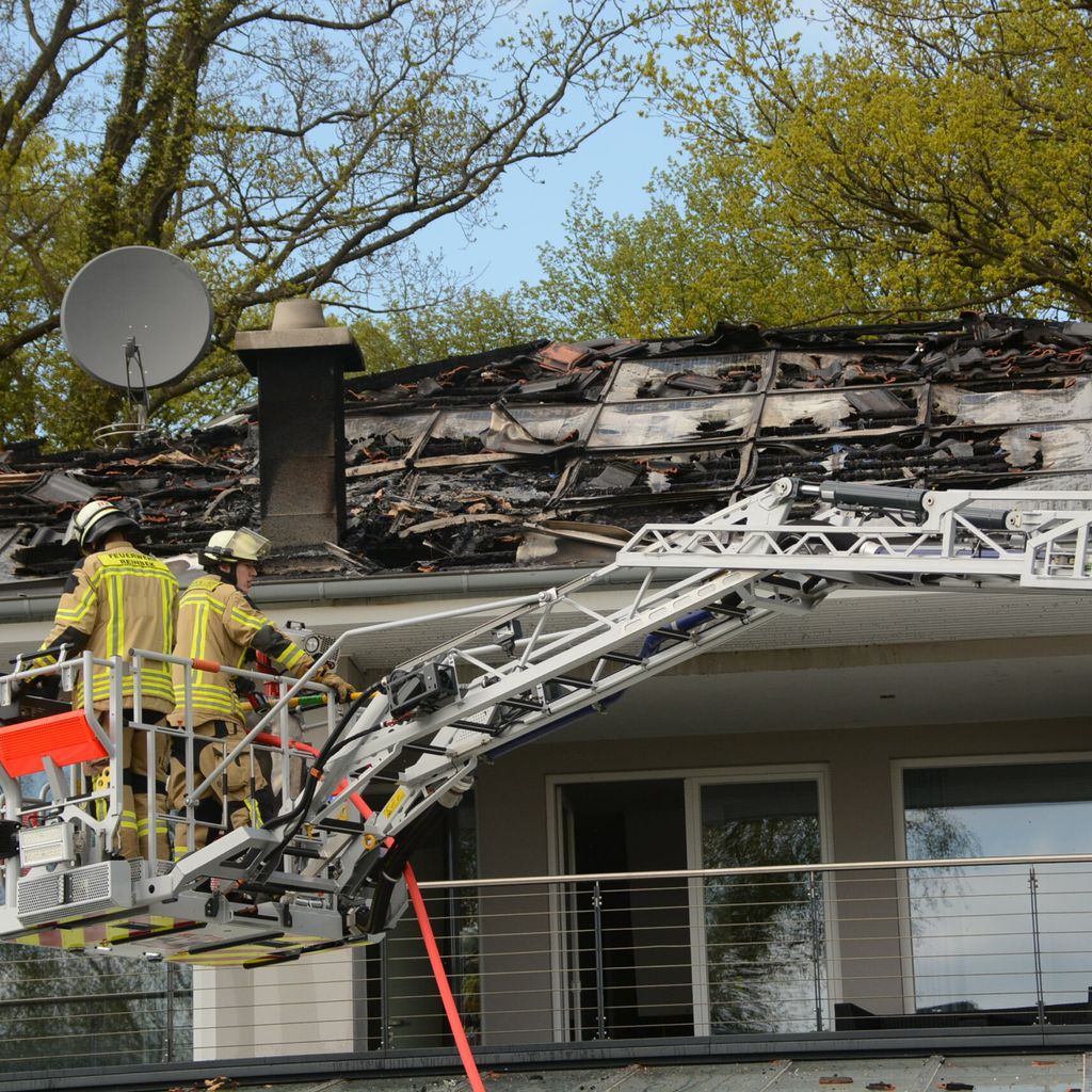 Feuerwehrleute stehen auf einem Kran vor dem ausgebrannten Dachstuhl.