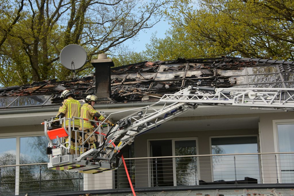 Feuerwehrleute stehen auf einem Kran vor dem ausgebrannten Dachstuhl.