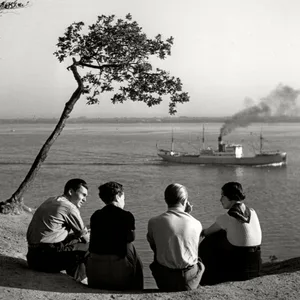 Schwarzweißfoto. Man sieht vier Menschen von hinten, die sich unterhalten. Im Hintergrund die ruhige Elbe, Rauch kommt aus dem Schlot eines kleines Dampfers