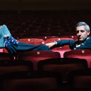 Abdollahi sitzt in einer Reihe mit roten Samt-Theatersesseln, die Füße auf der Lehne