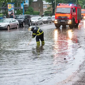 Eine Feuerwehrfrau steht in Billstedt auf einer von starkem Regen überfluteten Straße.