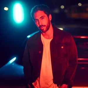 Max Giesinger von vorne fotografiert, es ist Nacht, dunkel, rot-orangenes Licht
