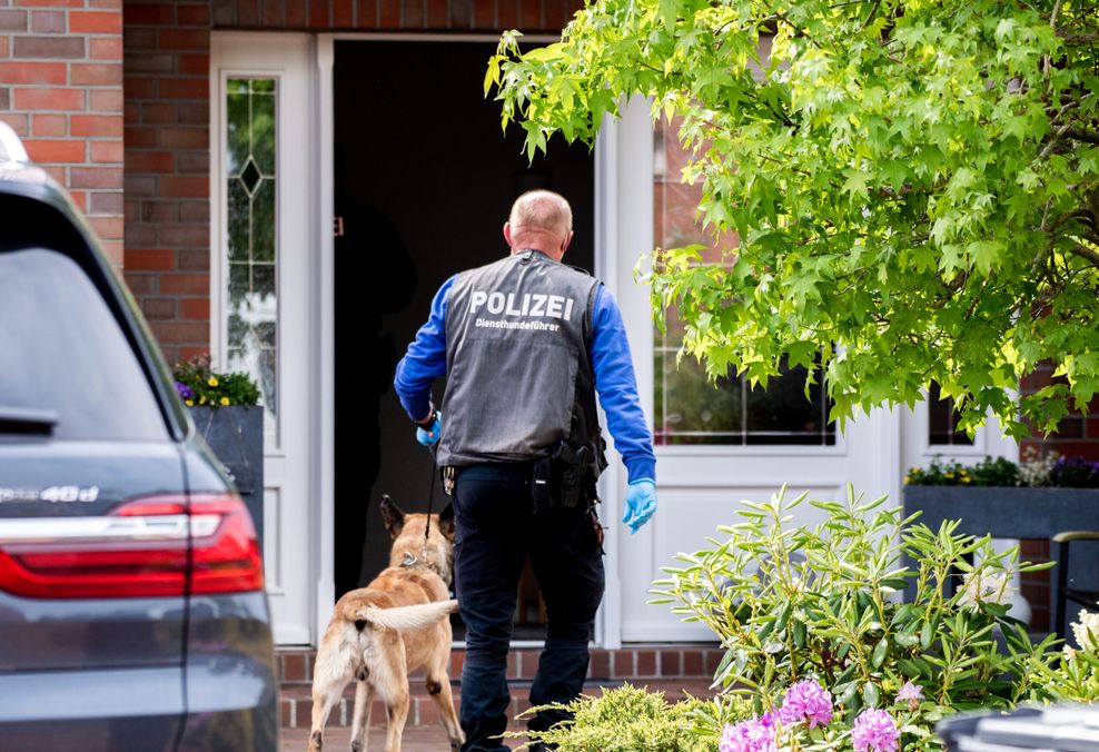 Ein Diensthundeführer der Polizei geht mit einem Spürhund zu einem Wohnhaus, das durchsucht wird.