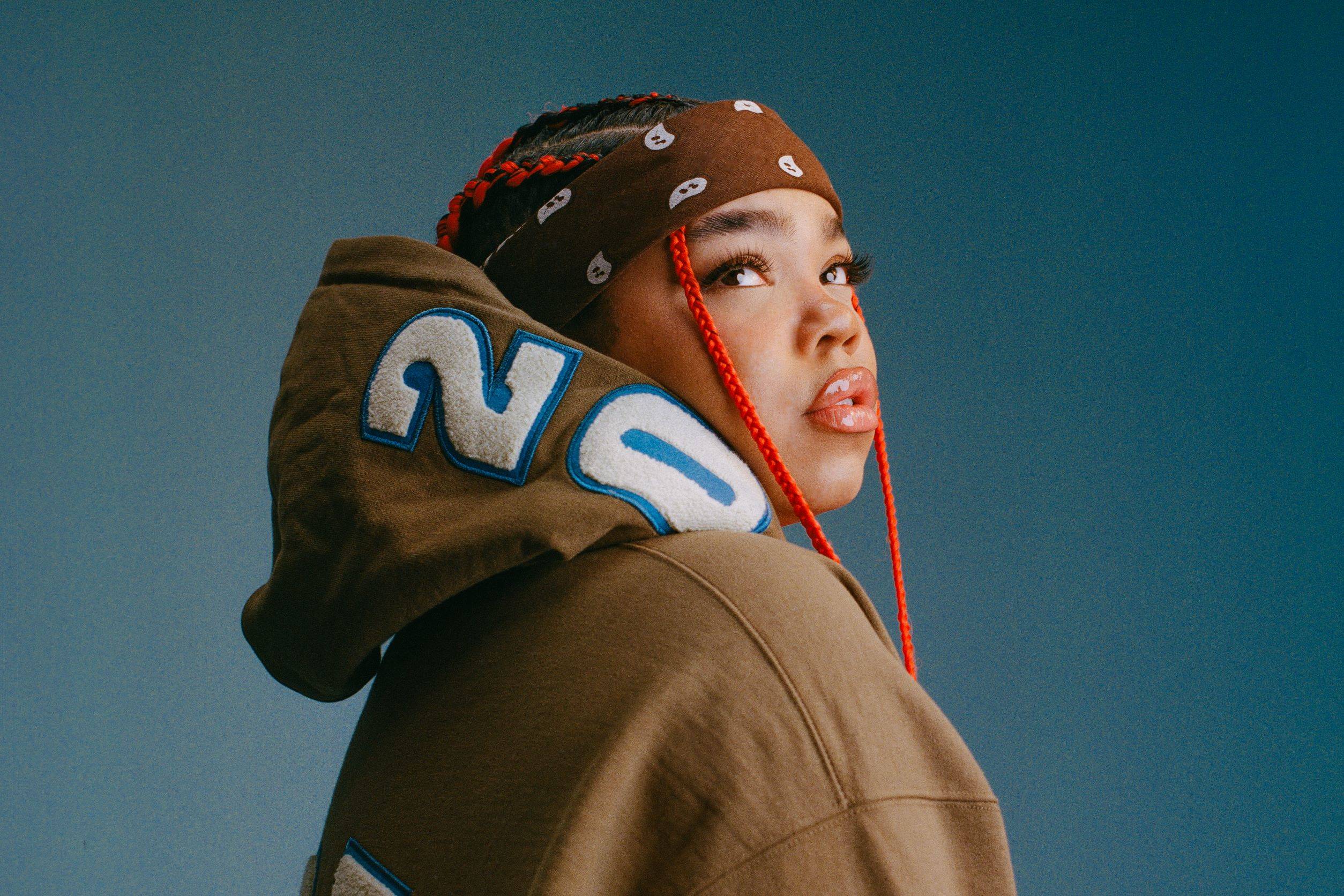 Zoe Wees ist von der Seite fotografiert, sie trägt einen braunen Hoodie und ein braunes Stirnband und schaut nach oben