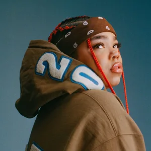 Zoe Wees ist von der Seite fotografiert, sie trägt einen braunen Hoodie und ein braunes Stirnband und schaut nach oben