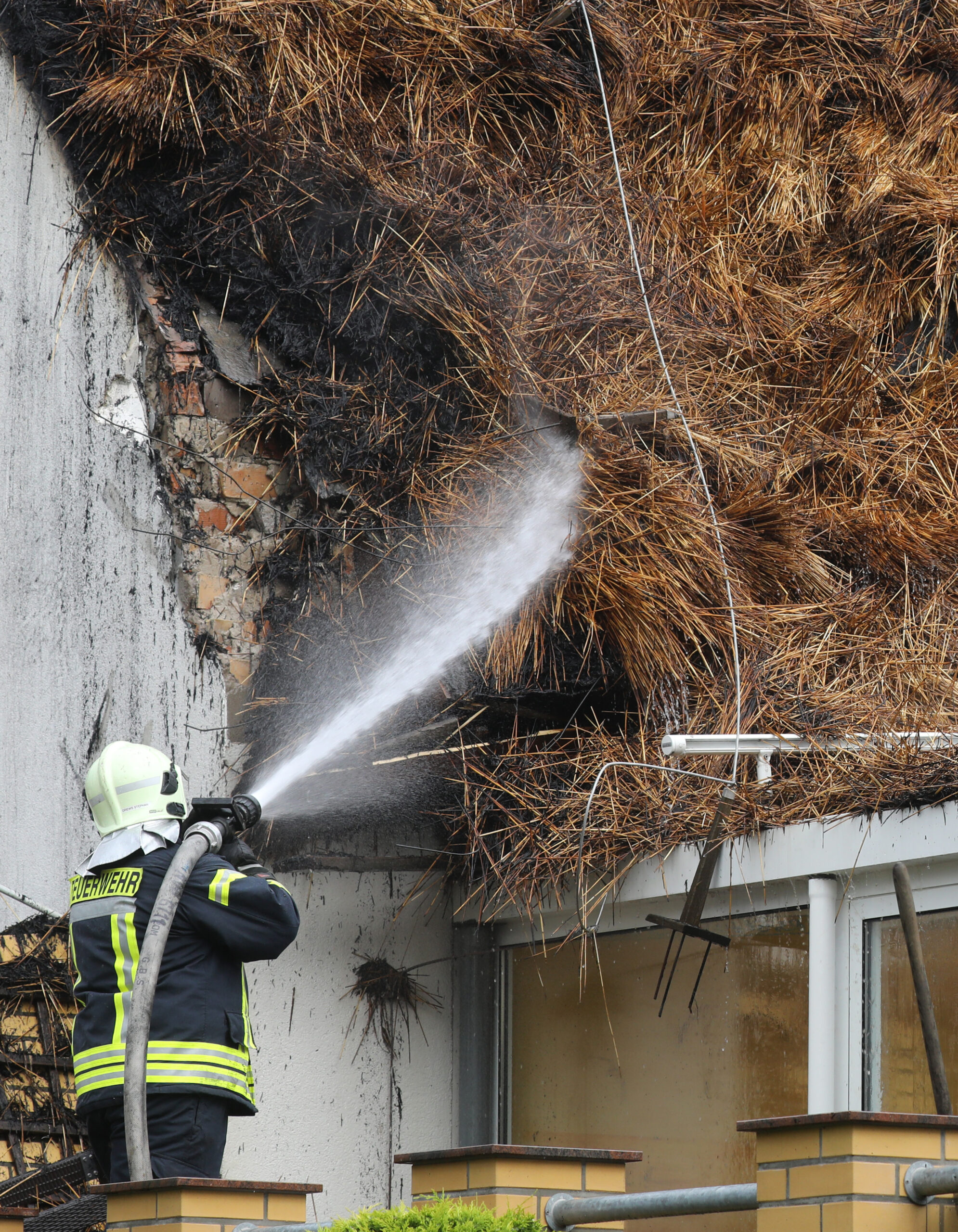 Ein Feuerwehrmann löscht ein Feuer auf einem Reetdach