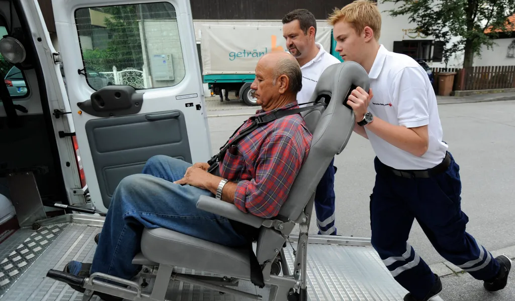 Ein Bundesfreiwilligendienstleistender schiebt einen älteren Herrn in einem Spezial-Rollstuhl.