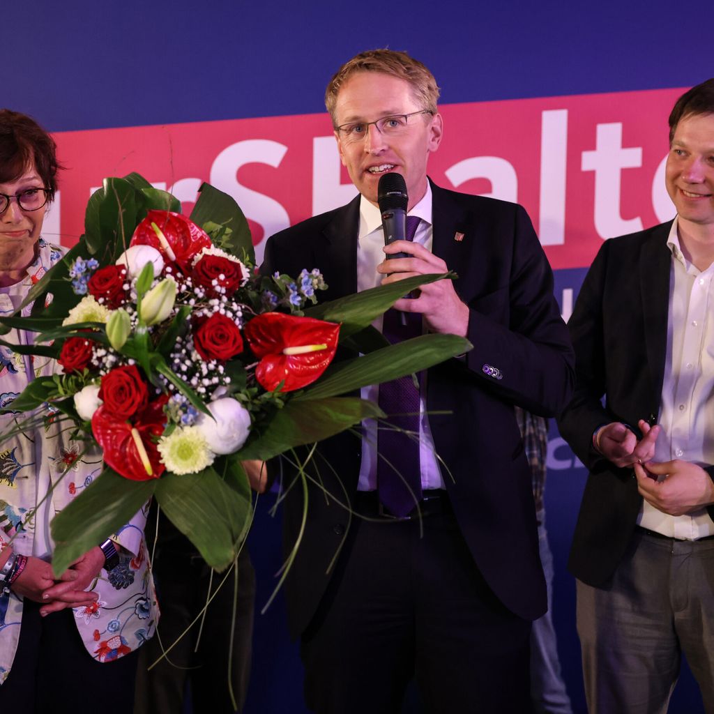 Günther steht umgeben von Partei-Kolleg:innen mit einem Blumenstrauß auf der Bühne.