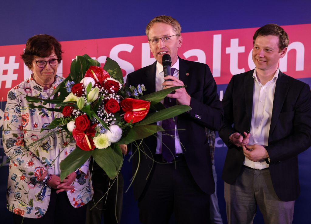 Günther steht umgeben von Partei-Kolleg:innen mit einem Blumenstrauß auf der Bühne.