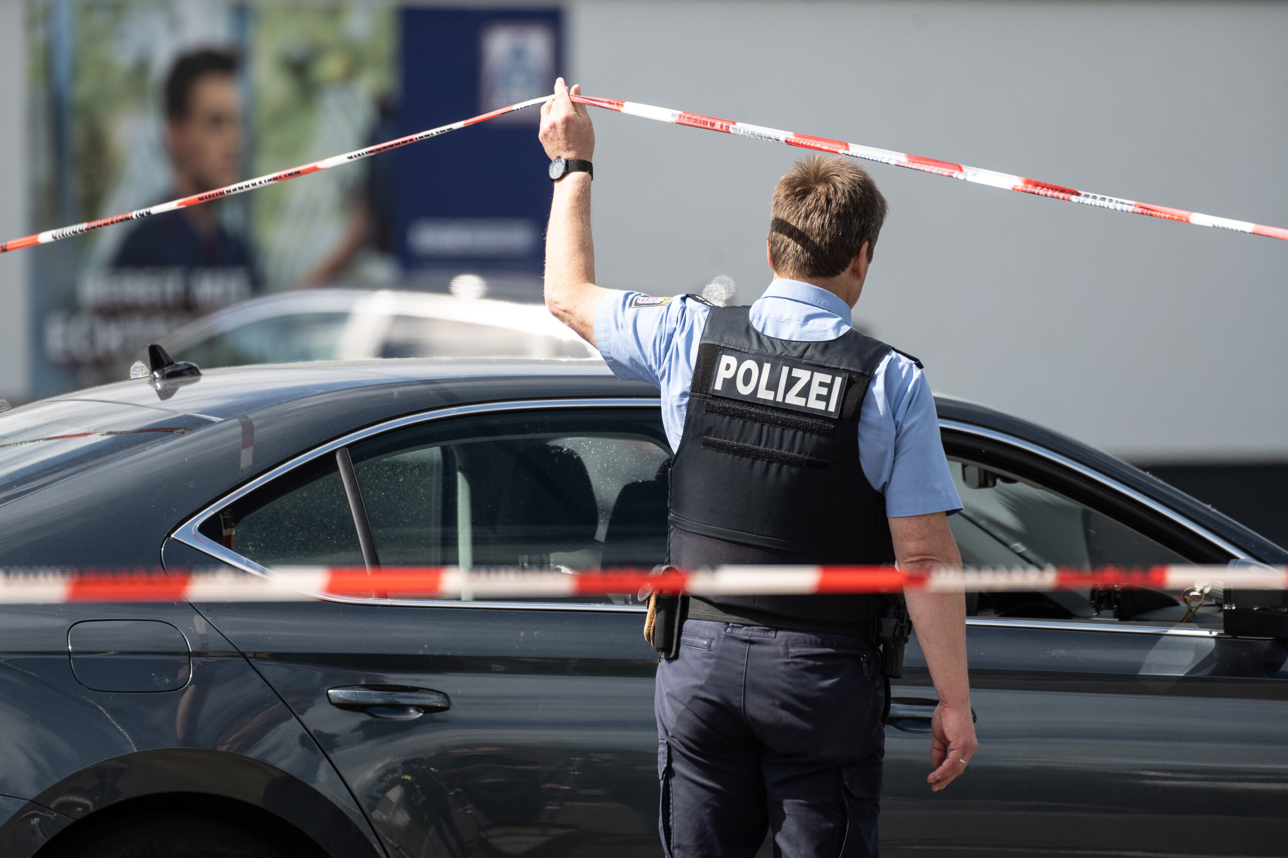 Ein Polizist geht unter einem Absperrband durch, das vor einem Einkaufsmarkt befestigt ist.