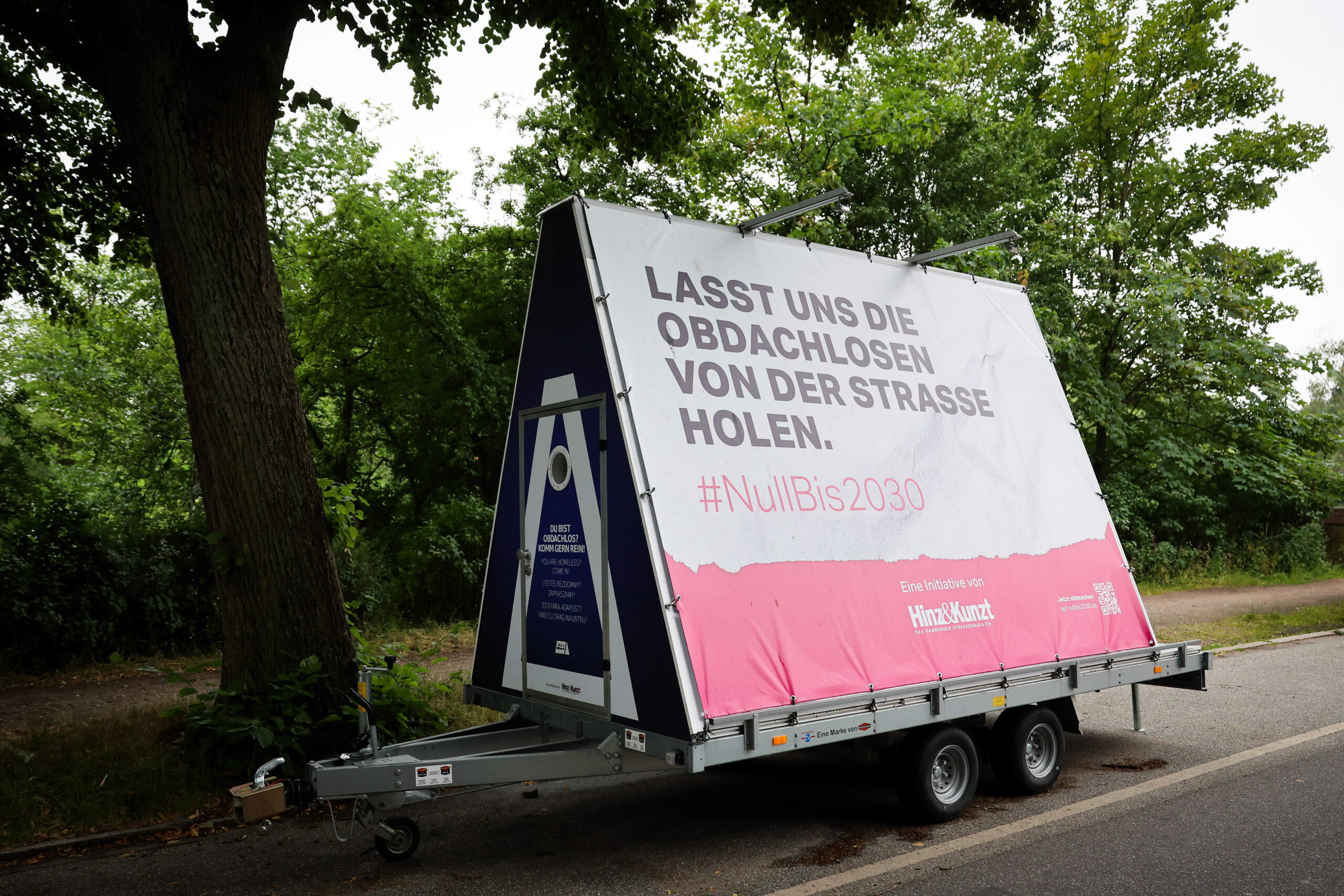 Ein Anhänger mit einer kleinen Unterkunft für Obdachlose steht an einer Straße am Stadtpark.