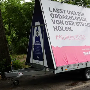 Ein Anhänger mit einer kleinen Unterkunft für Obdachlose steht an einer Straße am Stadtpark.