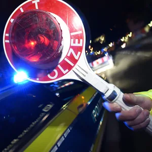 Symbolbild: Eine Polizeibeamtin hält vor einem Polizeifahrzeug mit Blaulicht eine Haltekelle in die Höhe