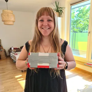 Marlin, eine blonde Frau mit langen Haaren, hat ein Paket in der Hand.