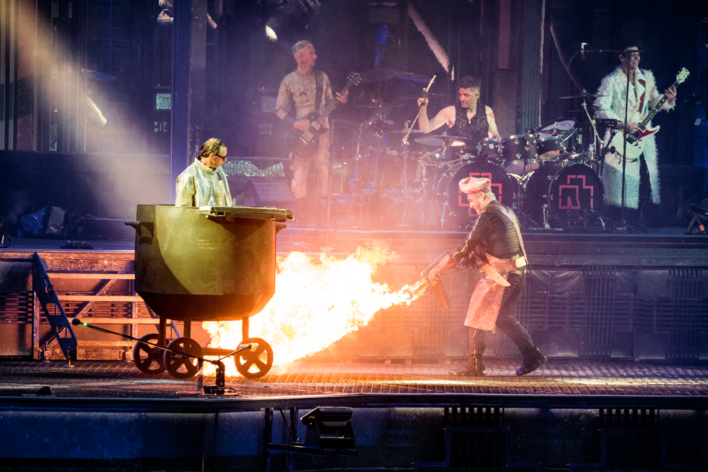 Lindemann mit einem Flammenwerfer neben einem großen Kochtopf, in dem ein Mann steht