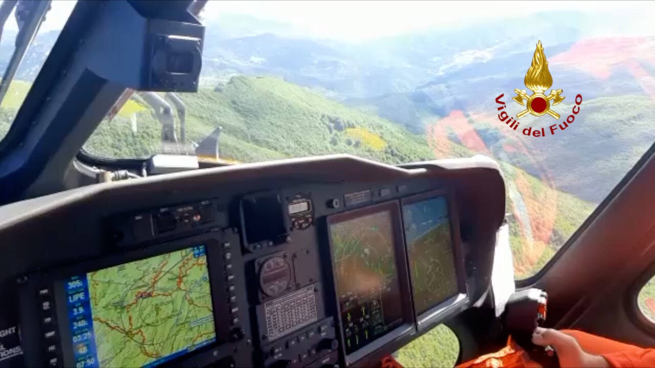 Ein italienischer Feuerwehrhubschrauber sucht die Absturzstelle eines Hubschraubers ab.
