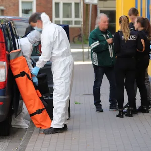 Ermittlerinnen und Ermittler befragen eine Person vor dem Haus, in dem sich der Doppelmord in Elmshorn ereignet hat.