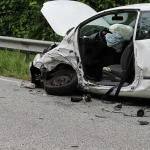 Ein zerstörtes weißes Auto steht am Fahrbahnrand