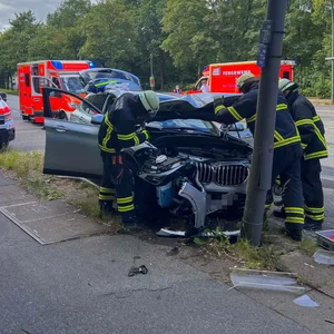 Feuerwehrkräfte begutachten den beschädigten BMW. Der Lichtmast ist durch den Unfall verbogen worden.