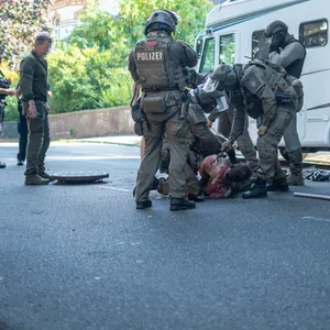Bewaffnete SEK-Beamte ziehen einen Mann aus der Kanalisation, ein Gully-Deckel liegt auf der Straße