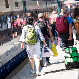 Reisende gehen auf der Nordseeinsel im Bahnhof Westerland an einem Zug der Deutschen Bahn entlang.