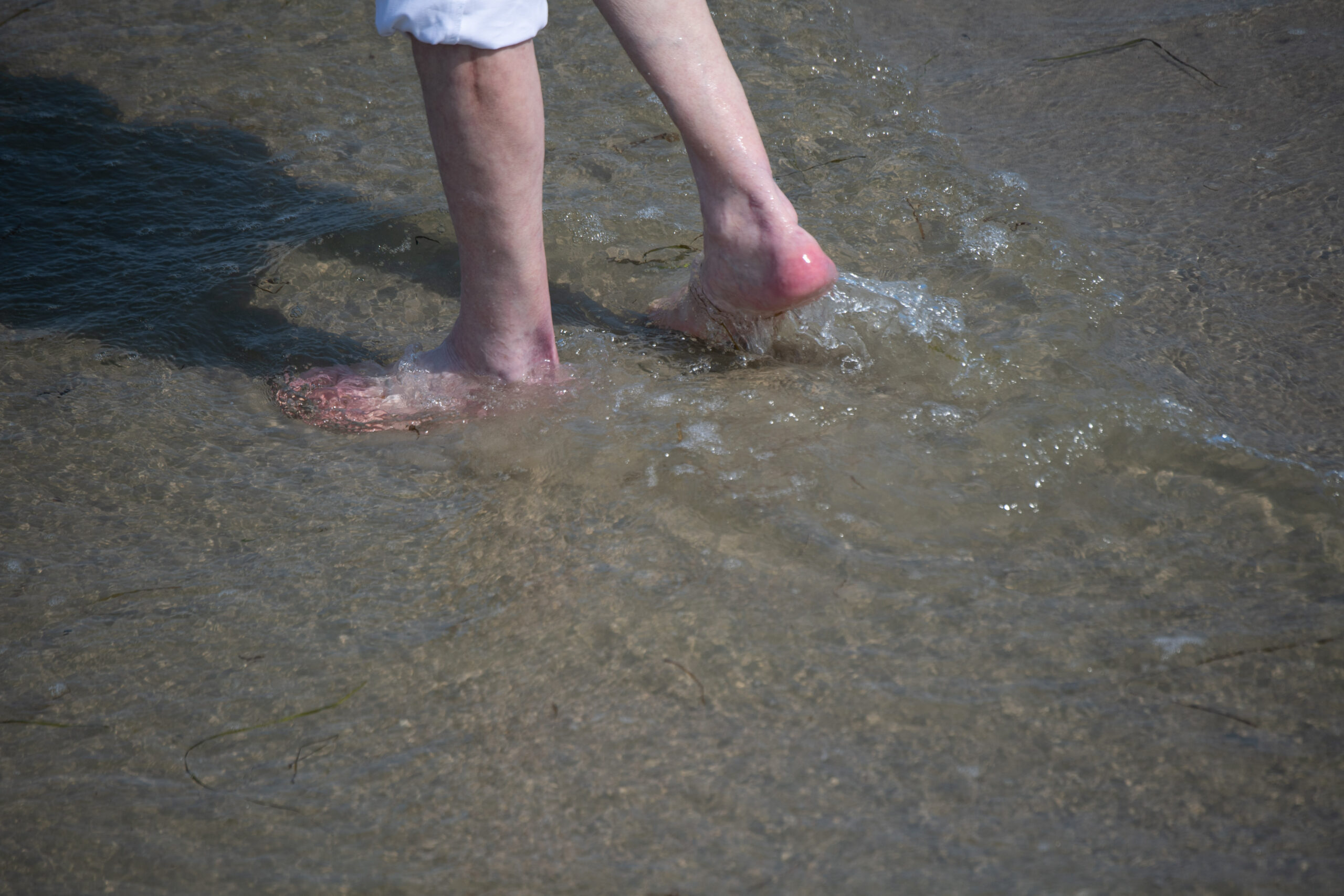 Ein Mann watet durch das flache Wasser am Strand eines Seebads.