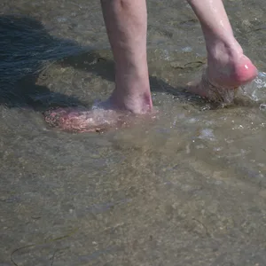 Ein Mann watet durch das flache Wasser am Strand eines Seebads.