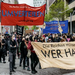 Demonstrant:innen halten Schilder mit Forderungen zu finanzieller Umverteilung.