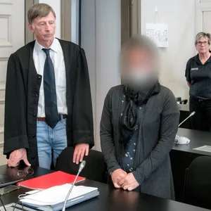 Eine kleine Frau steht zwischen ihren Verteidigern. Ihr Gesicht wurde unkenntlich gemacht.