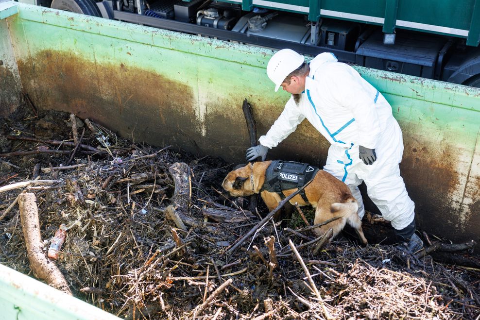 Ein Polizist durchsucht mit einem Leichenspürhund einen Container mit Treibgut.