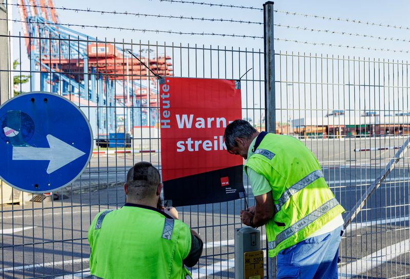 Hafenarbeiter hängen am Zaun der Containerterminals der HHLA (Hamburger Hafen und Logistik AG) ein Schild mit der Aufschrift „Warnstreik“ auf.