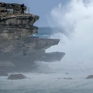 Menschen stehen auf einem Felsvorsprung, während riesige Wellen auf die Landzunge am Bondi Beach in Sydney, Australien, treffen.