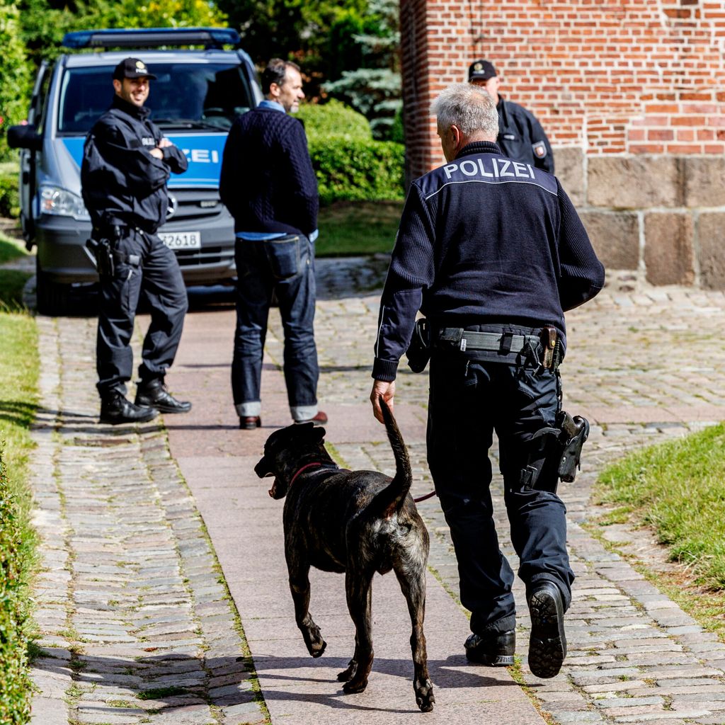 Polizisten mit Spürhund vor einem Polizeiwagen.