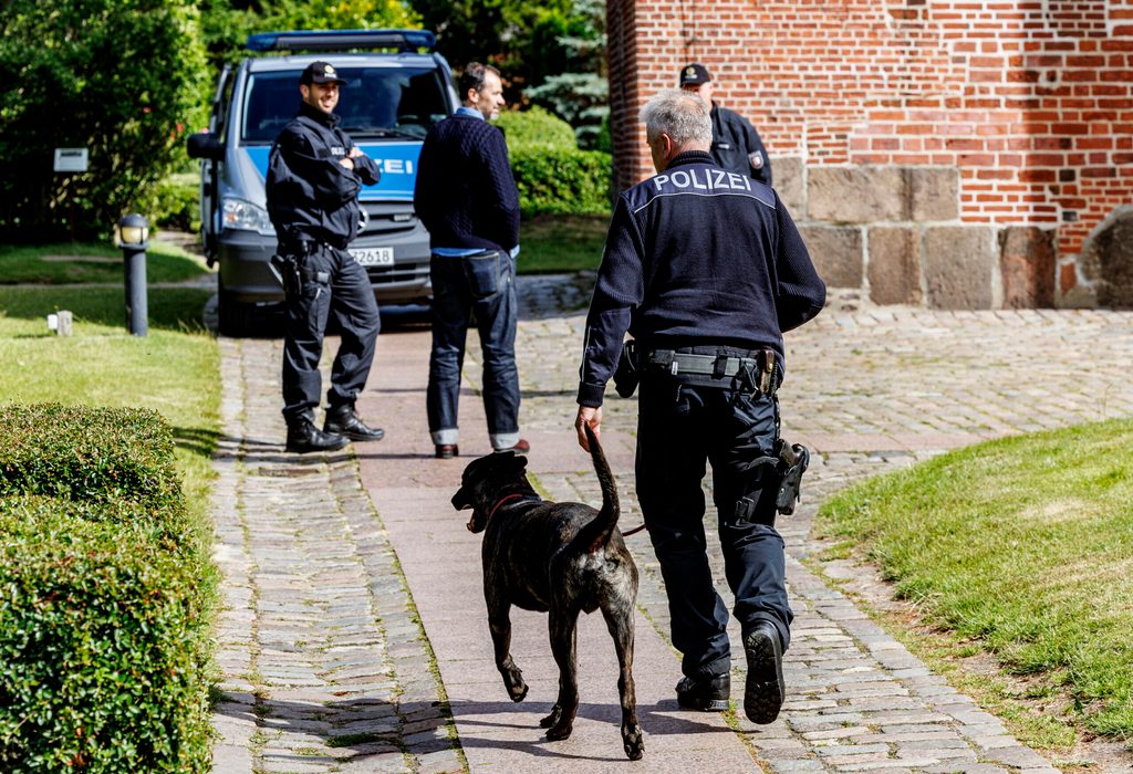 Polizisten mit Spürhund vor einem Polizeiwagen.