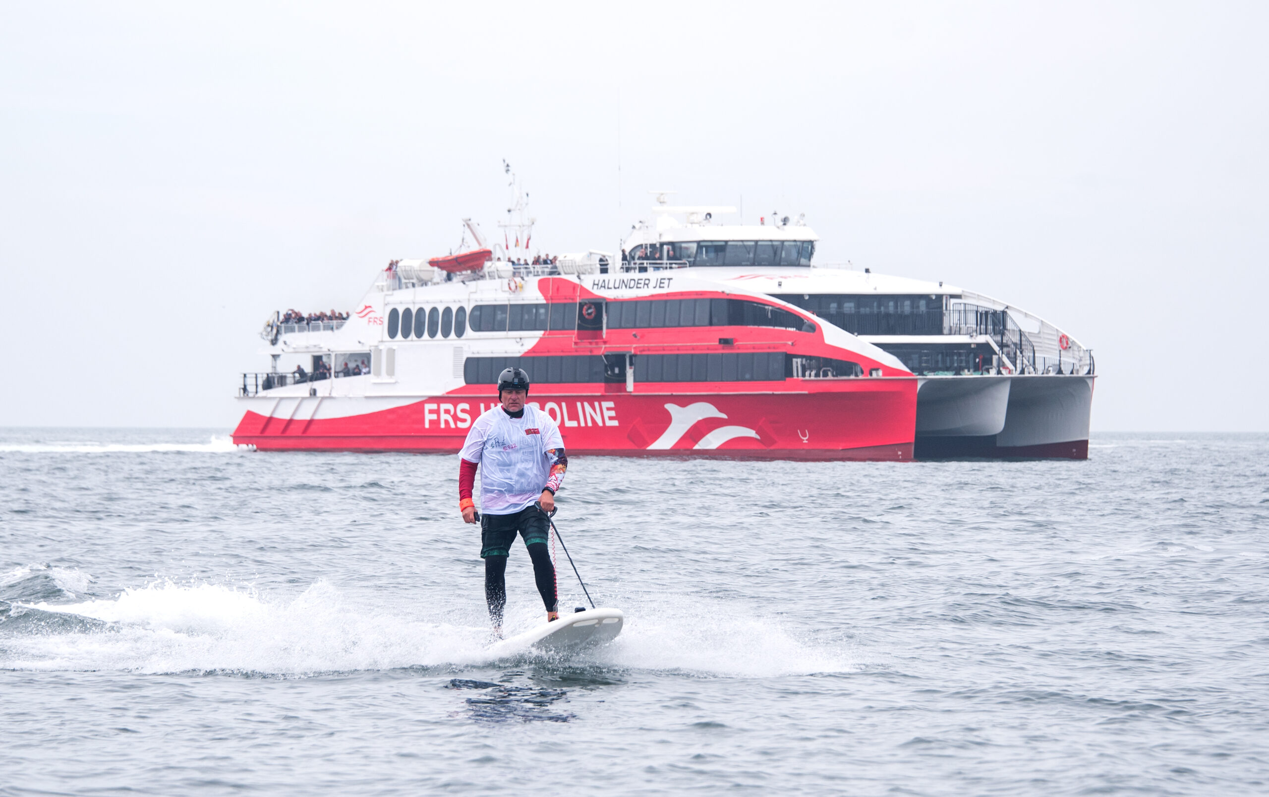 Jörg Singer, Bürgermeister der Insel Helgoland, fährt im Rahmen einer Aktion gegen Plastikmüll im Meer auf einem E-Surfboard neben dem Katamaran „Halunder Jet”.