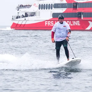 Jörg Singer, Bürgermeister der Insel Helgoland, fährt im Rahmen einer Aktion gegen Plastikmüll im Meer auf einem E-Surfboard neben dem Katamaran „Halunder Jet”.