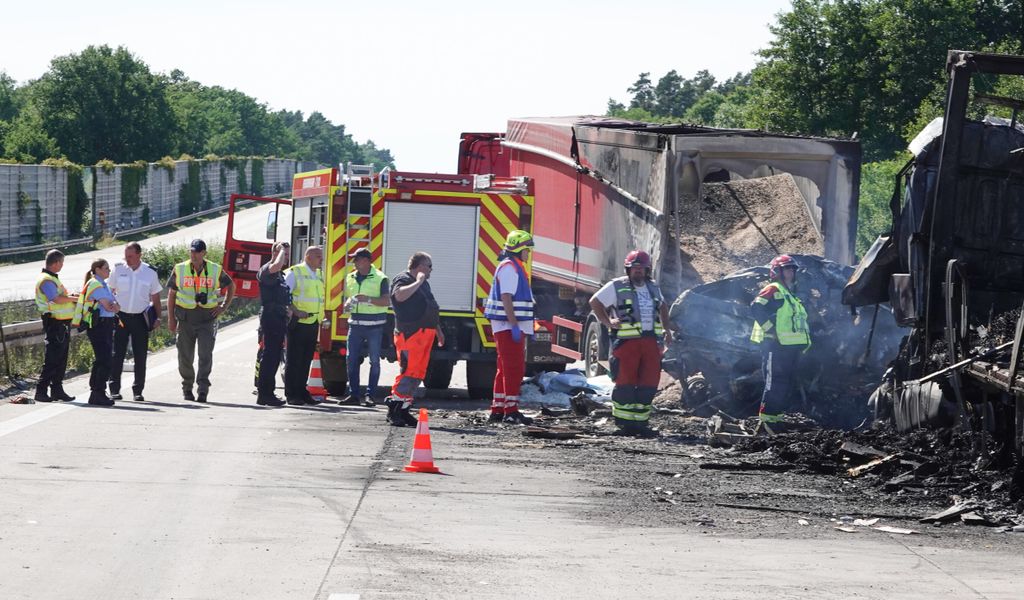 Rettungskräfte stehen auf der Autobahn neben zerstörten Lkw