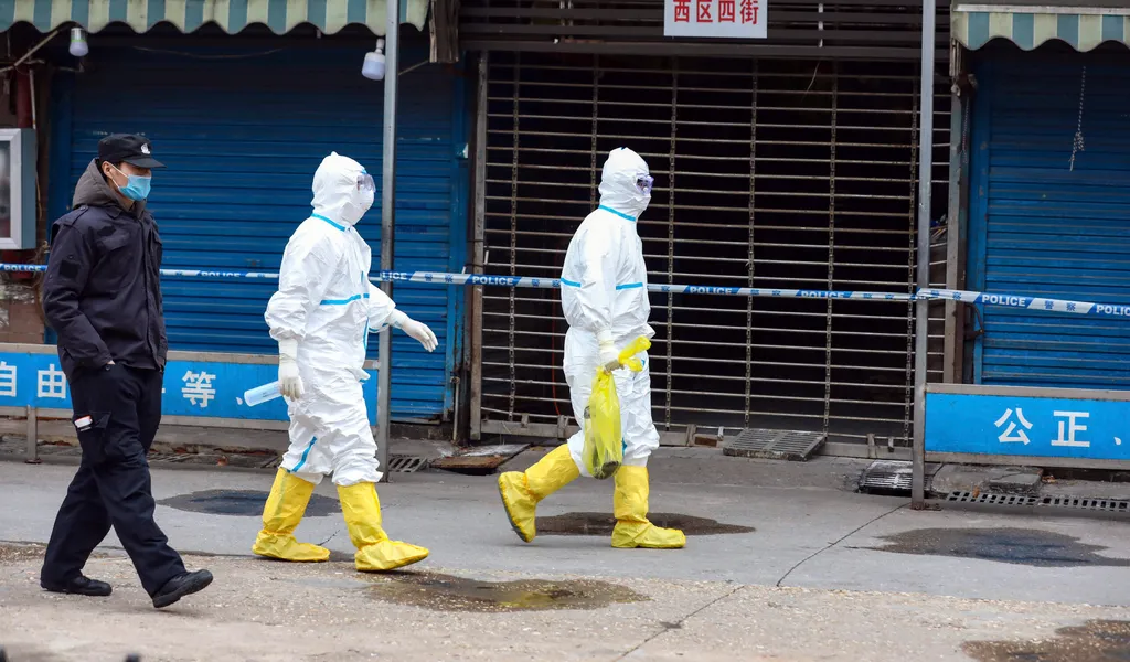 Zwei Männer in virologischen Schutzanzügen gehen durch eine leere Straße